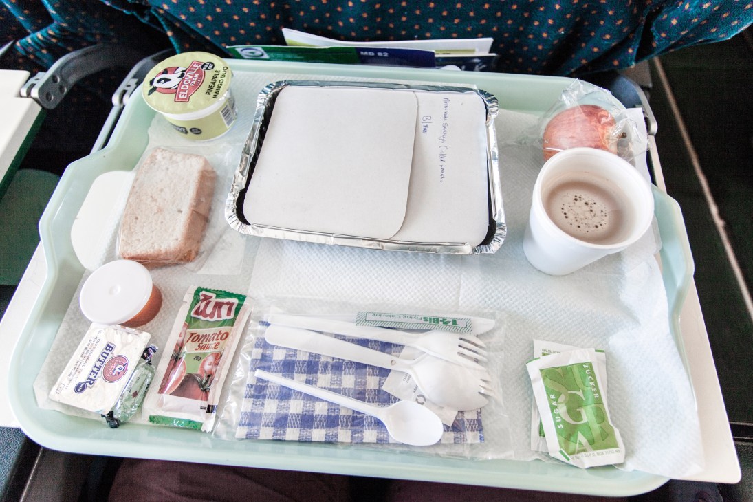 African Express business class meal tray with sausage, baked beans, sponge cake, butter, tomato sauce, and Nescafé coffee.