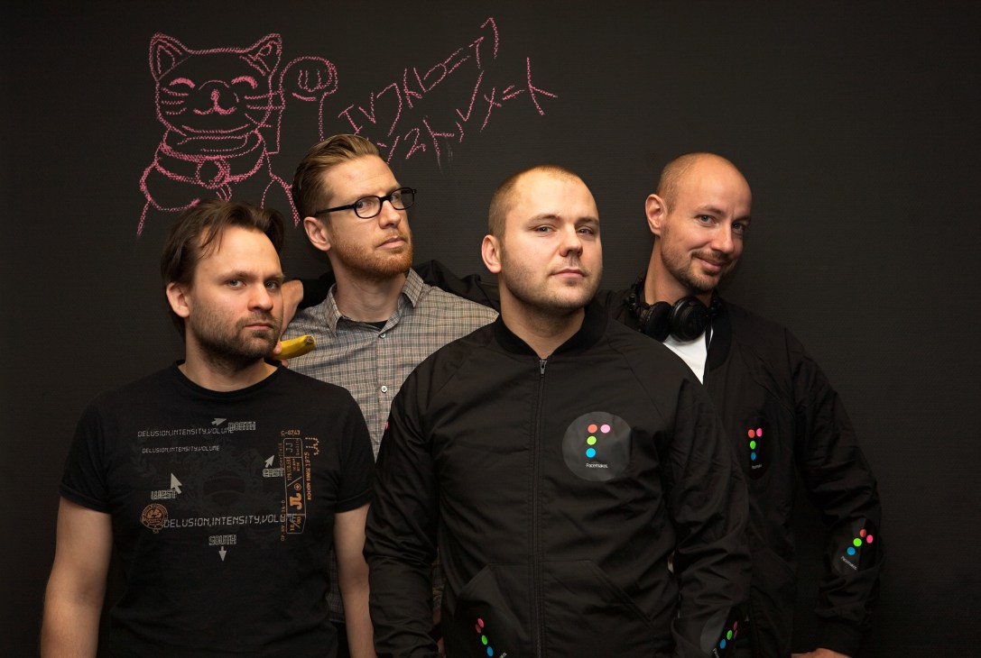 Four men pose against a dark background with neon pink drawings, two wearing Pacemaker-branded clothing.