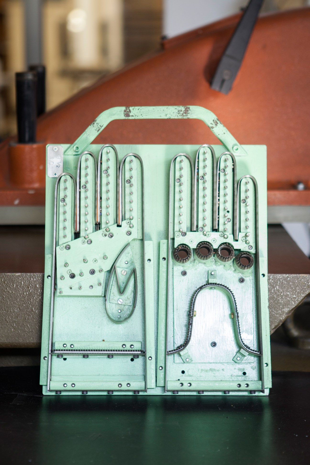 A green metal glove press with multiple curved dies and metal rivets used to cut leather.