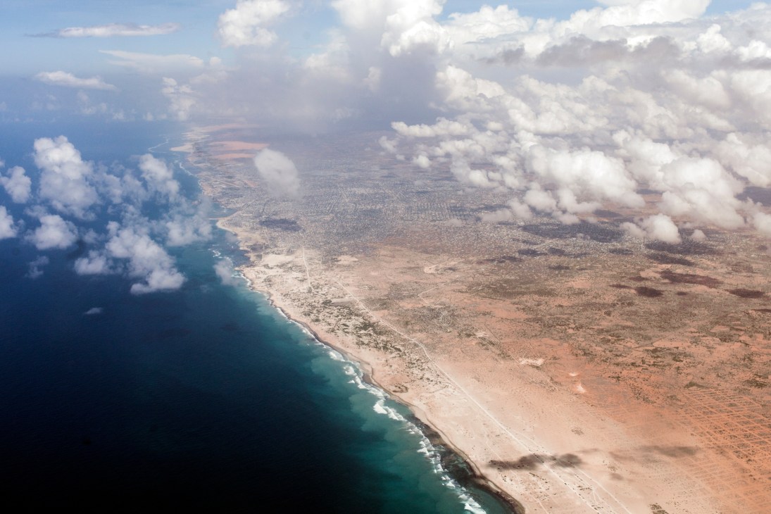 Aerial view of the Somali coastline showing turquoise waters meeting arid desert terrain with white clouds.