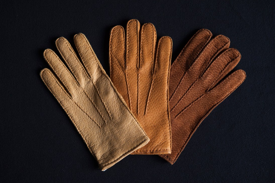 Three pairs of Restelli leather gloves in cream, tan and brown peccary leather displayed on dark background.