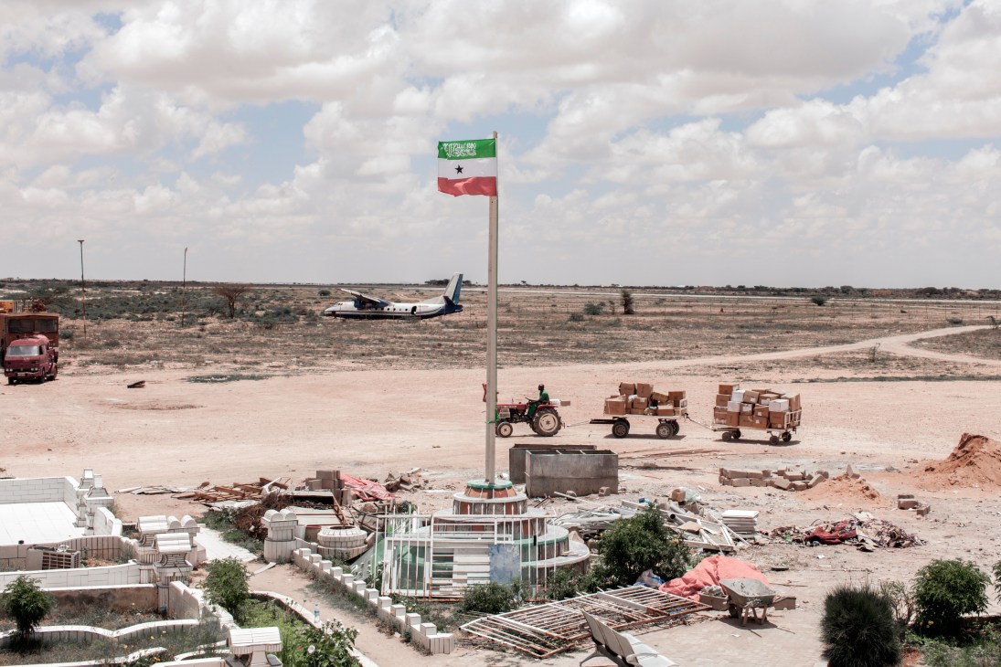 Somaliland flag flying above Hargeisa airport with aircraft and cargo vehicles on desert runway.