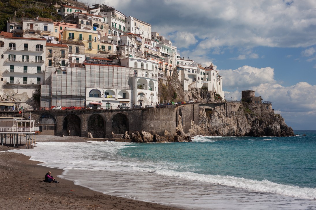 Colorful buildings cascading down a cliff overlooking Amalfi's beach and turquoise bay.