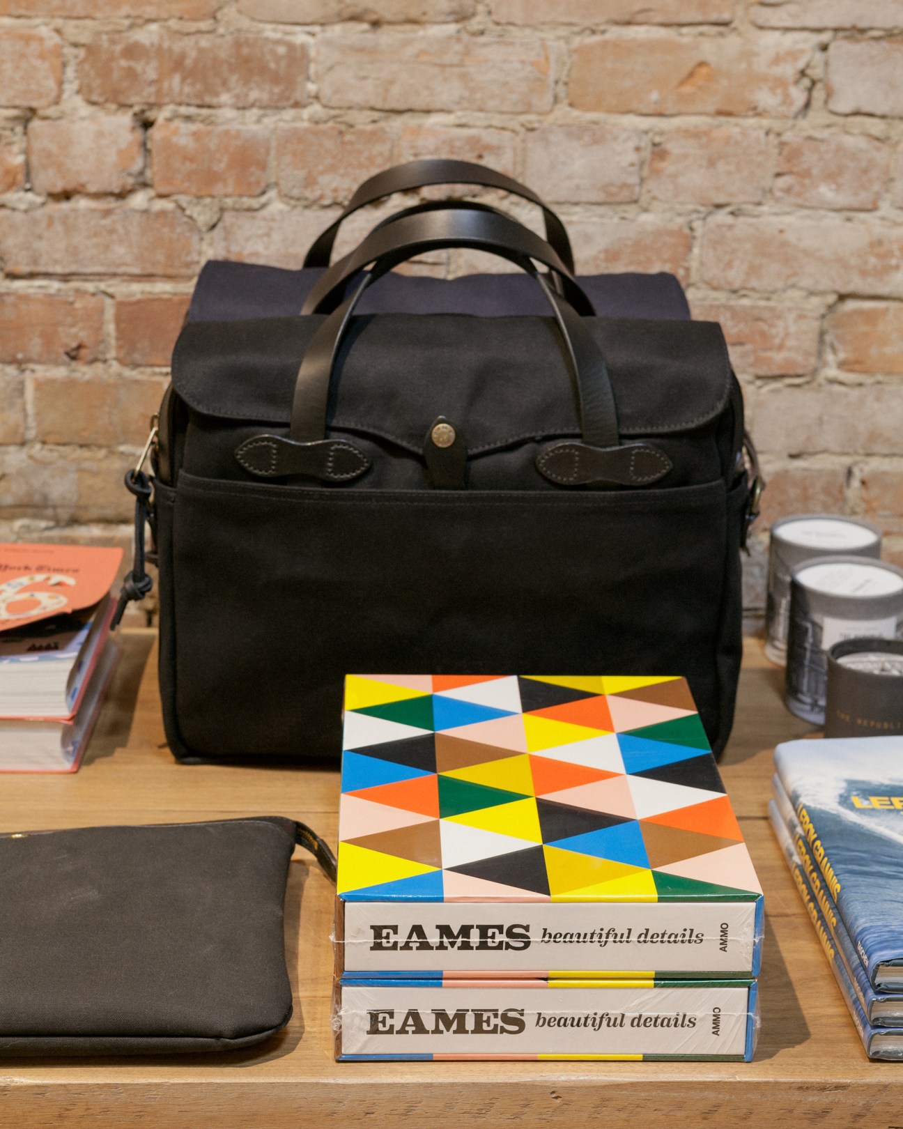 Black leather handbag displayed on wooden table with design books and accessories against brick wall at Rooney boutique.