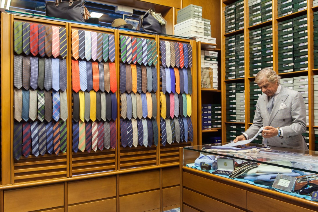 Man examining necktie samples displayed in wooden cabinets at Petronius showroom.