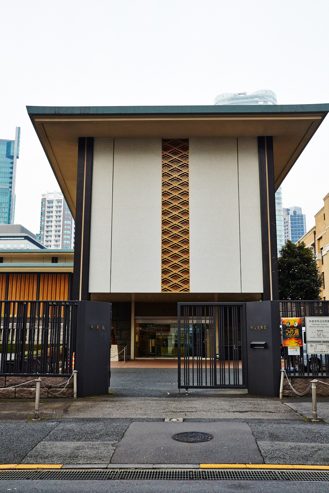 Modern Japanese government building entrance with white facade, wooden lattice detail, and black gates.