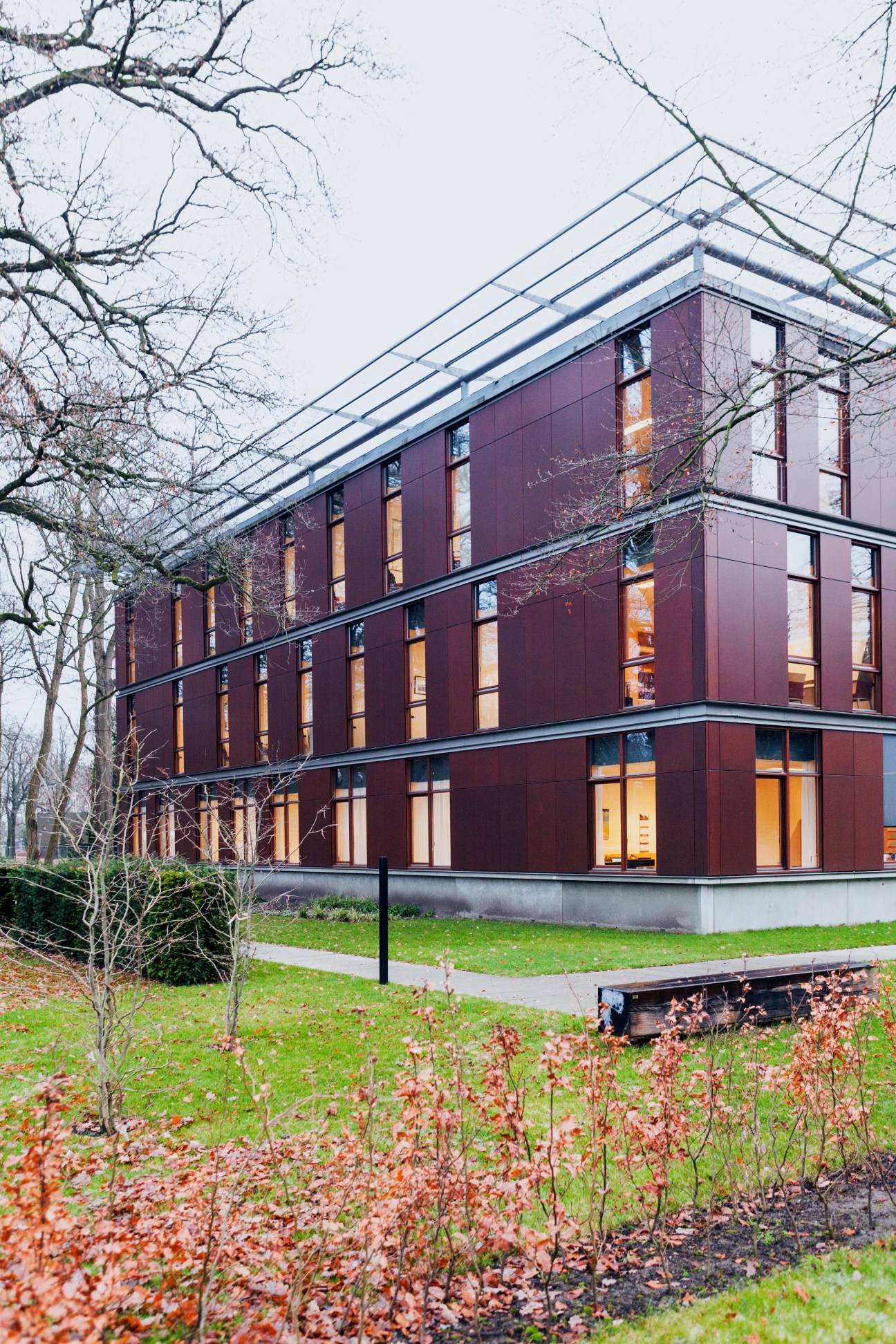Modern brick building with large windows and metal roof surrounded by bare trees and winter foliage.