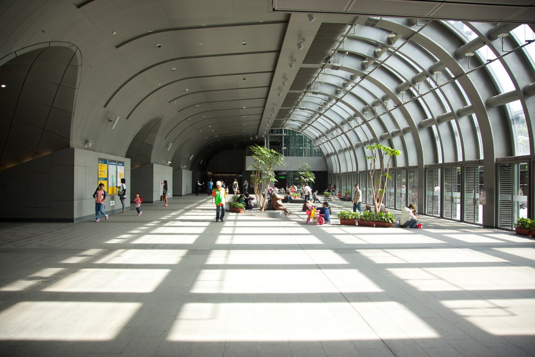 Interior of Da'an Park Station with curved ceiling, natural light, plants, and people walking through spacious platform.