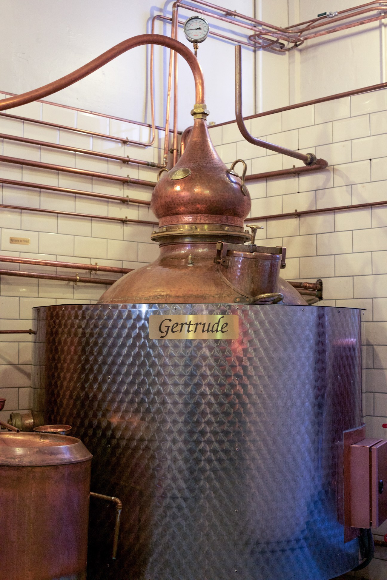 Copper pot still named Gertrude used in whisky distillation, with connected pipes and pressure gauge.
