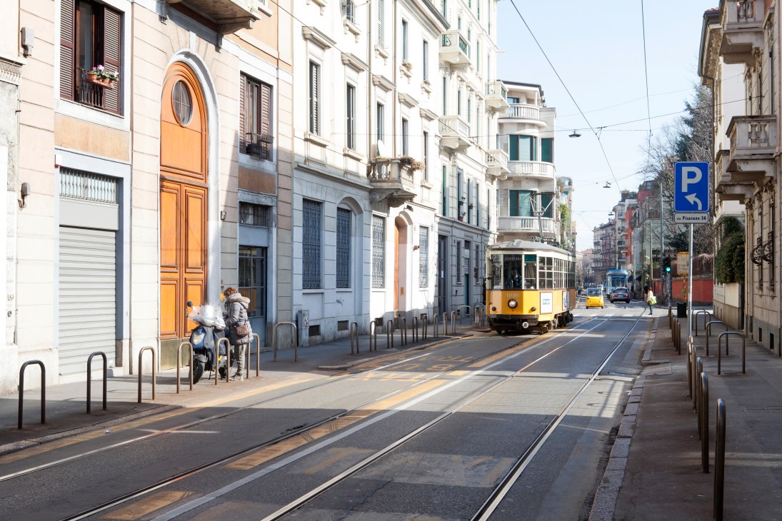 Yellow tram on tracks in a Milan street with historic buildings and a cyclist in the Porta Venezia district.