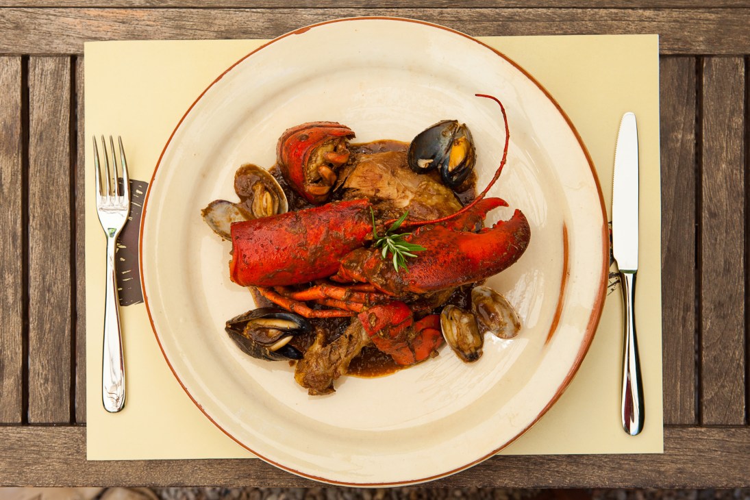 Mar y montaña dish from Hostal Sa Rascassa featuring lobster, chicken, clams and mussels on a white plate with red rim.