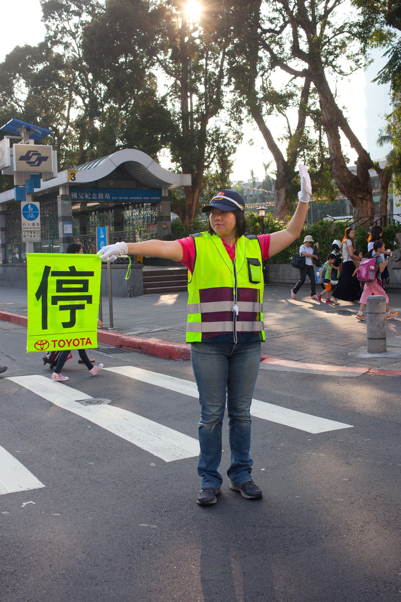 Traffic guard in neon yellow safety vest holding a stop sign at a Taipei street crossing.