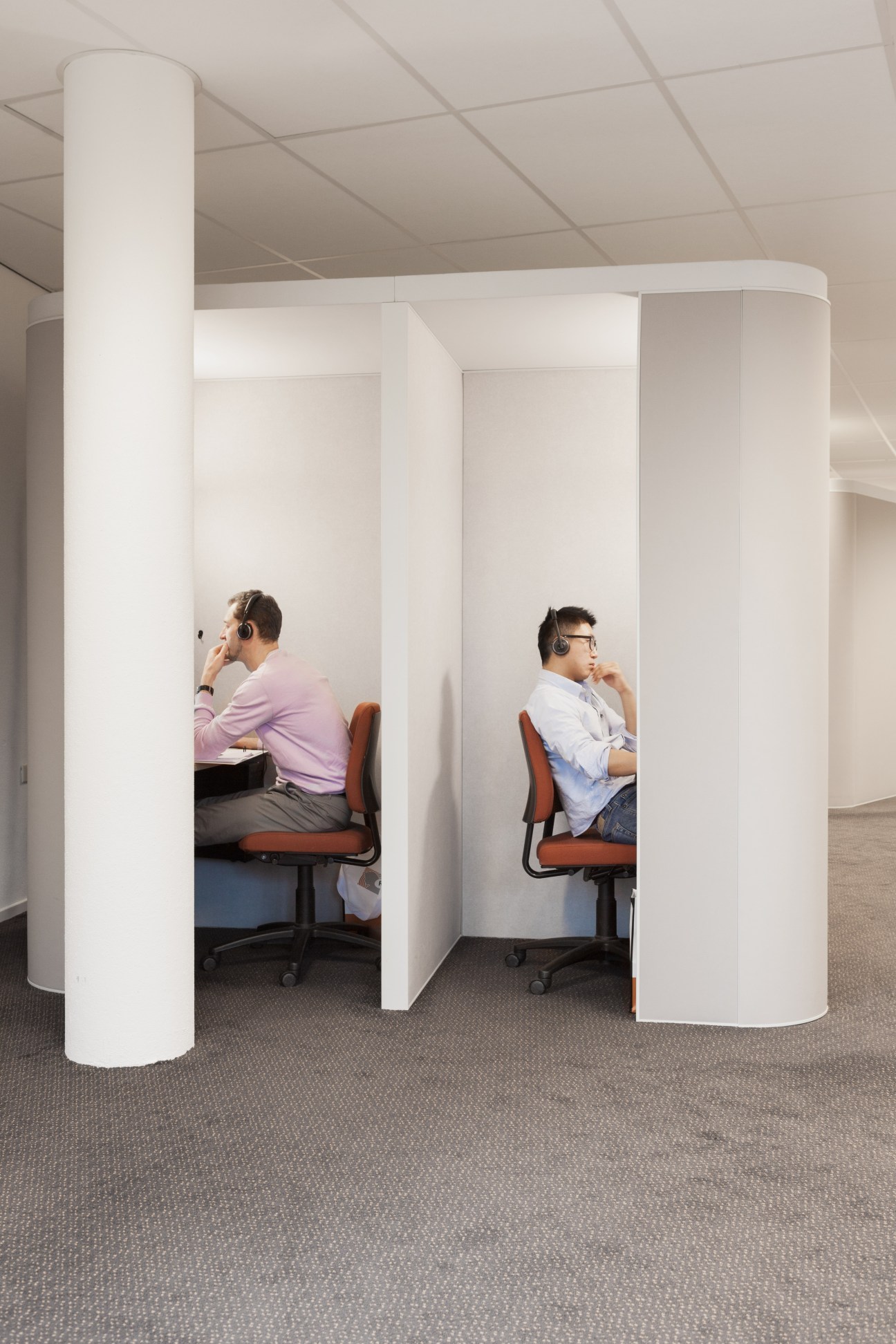 Two students wearing headphones sit in separate white audio study booths at Regina Coeli language institute.