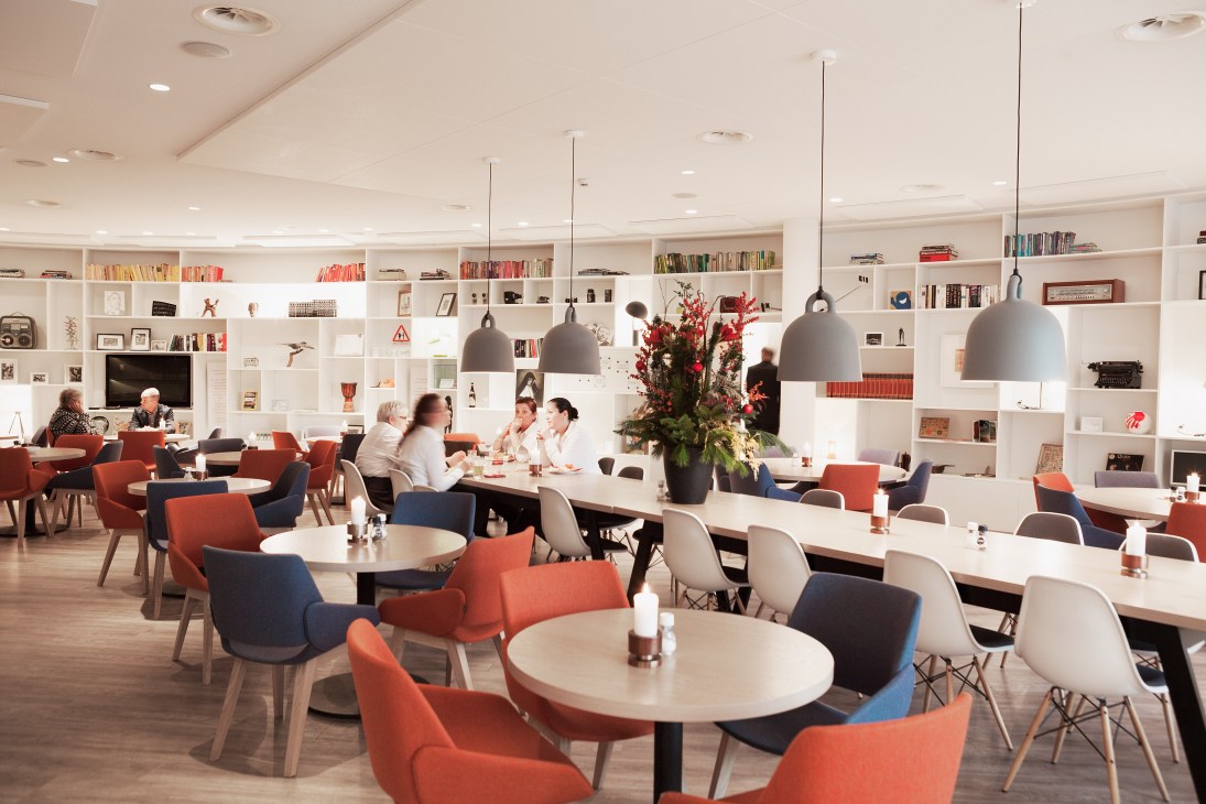Modern canteen with colorful chairs, pendant lights, and white shelving filled with books and decorative items at Regina Coeli language school.