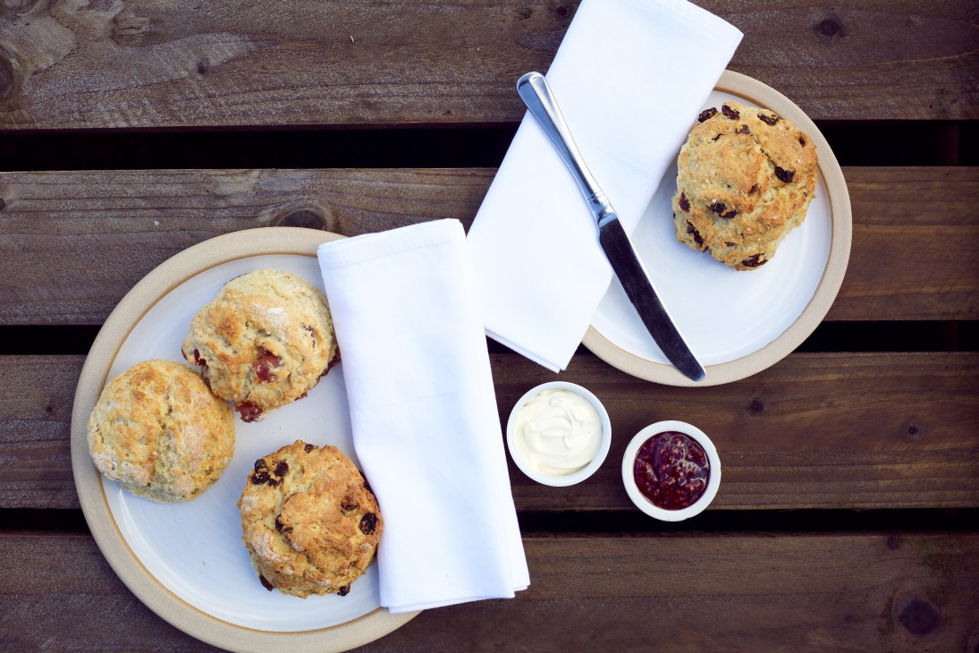 Scones with cream and jam served on plates with napkins on a wooden table at Balgove Larder café.