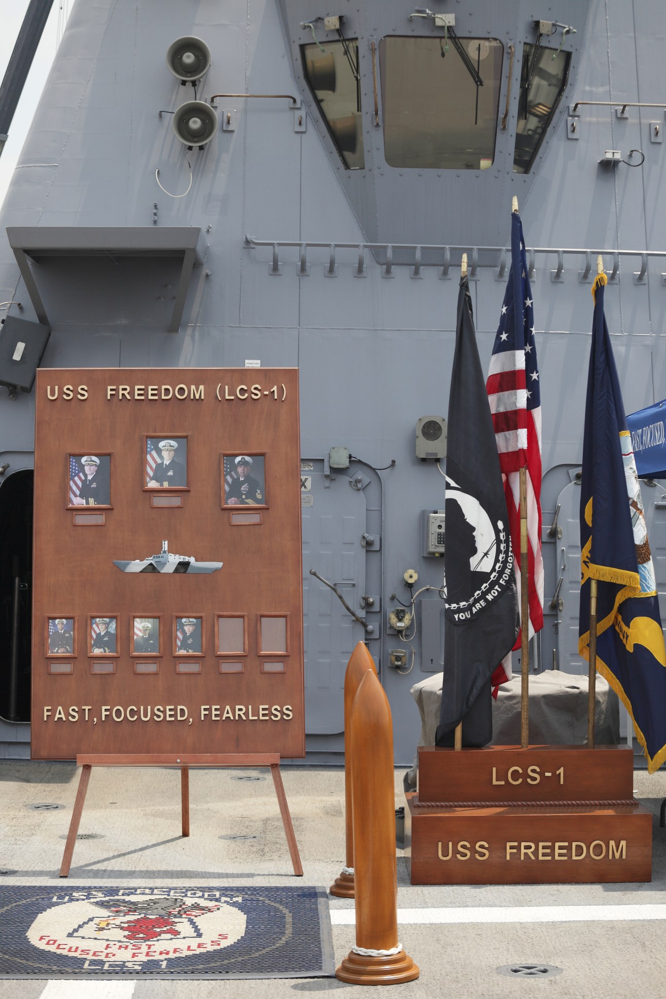 USS Freedom ship's dedication display with personnel portraits and flags on deck.
