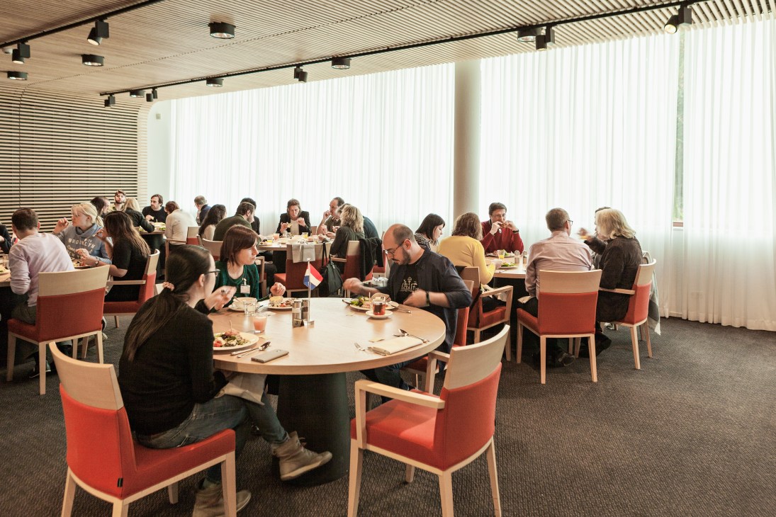 Students eating lunch together in a bright dining room with round tables and red chairs at Regina Coeli language institute.