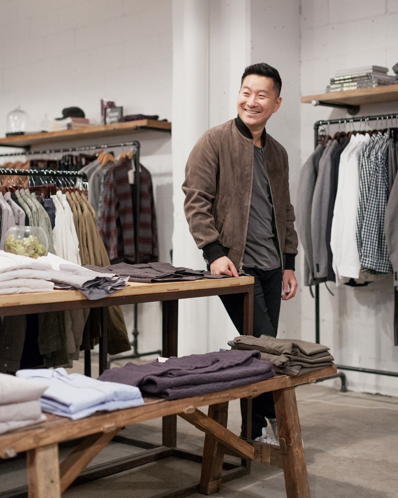 Ethan Song, CEO of Frank & Oak, stands smiling in a minimalist retail space with clothing displays and wooden tables.