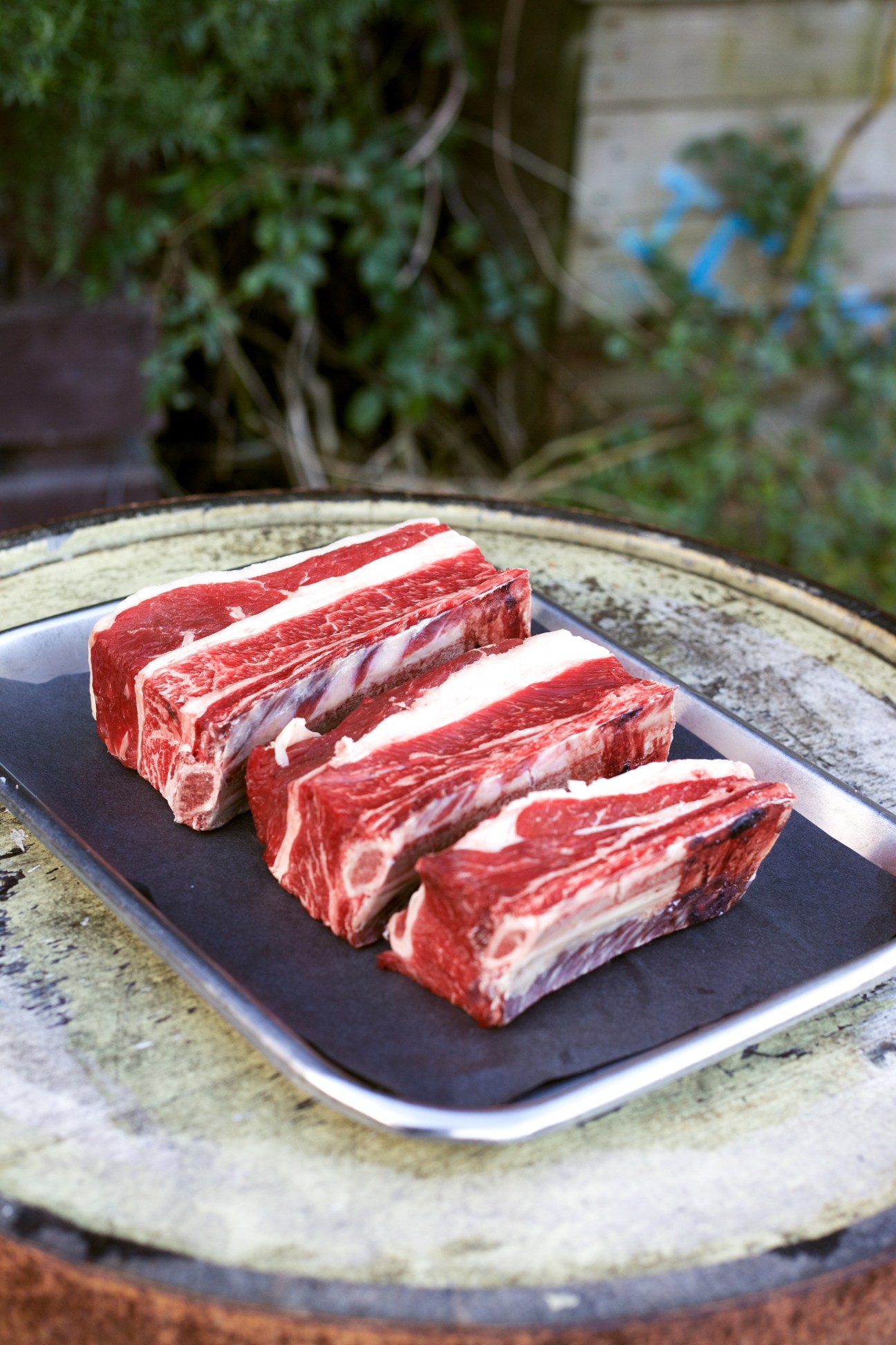 Raw beef short ribs with marbling displayed on a dark plate outdoors