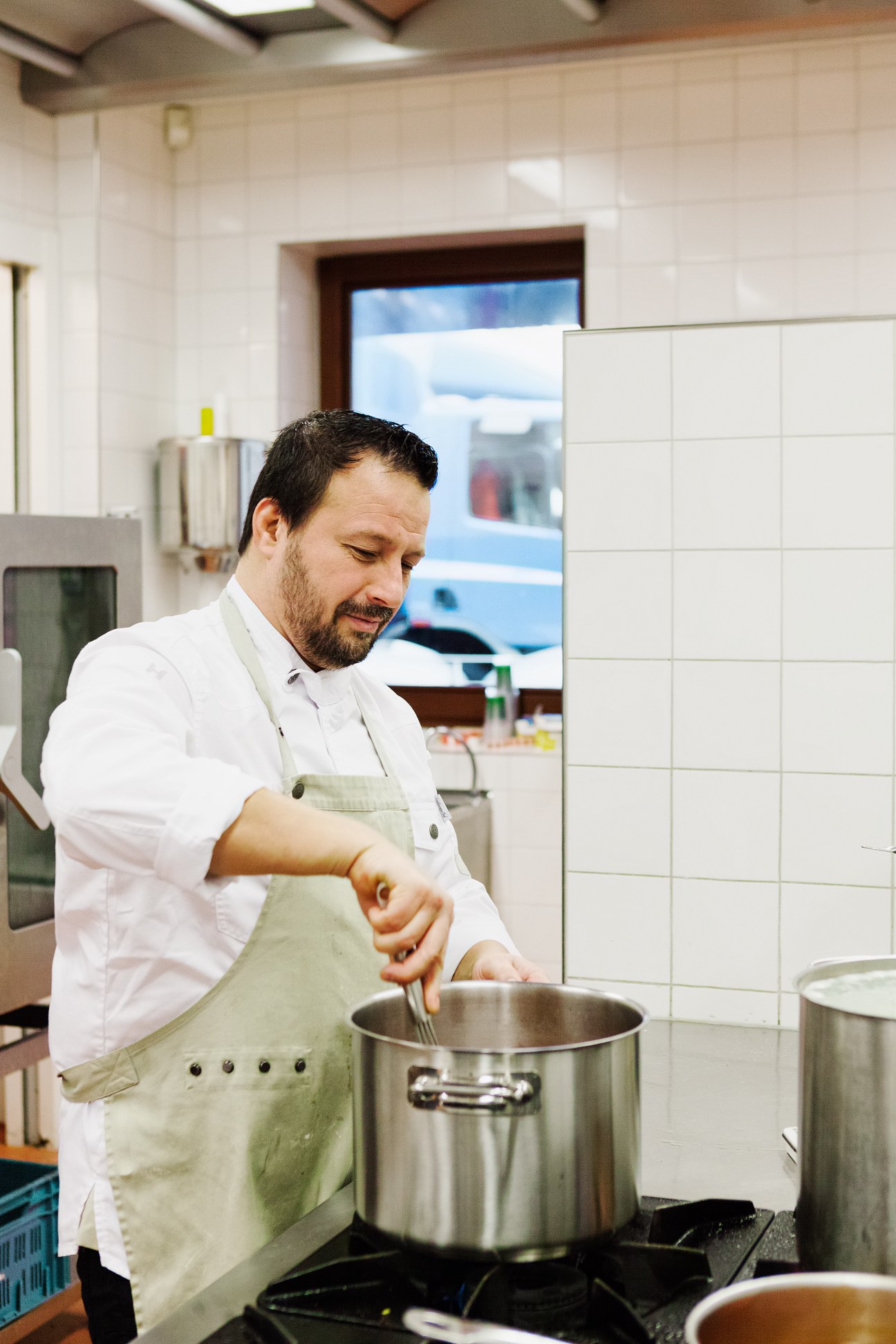 School chef Danny van der Vorm stirring a large pot in a white tiled kitchen.