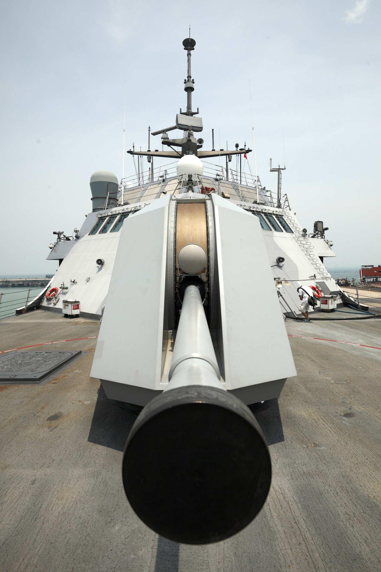 Overhead view of USS Freedom's Bofors Mk-110 57mm gun and sleek white hull at dock.