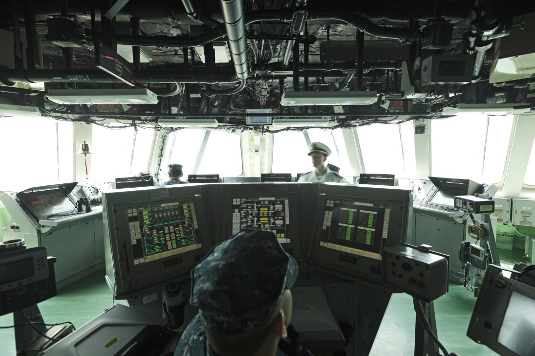 The wheelhouse of USS Freedom with three naval officers operating navigation systems and electronic displays.