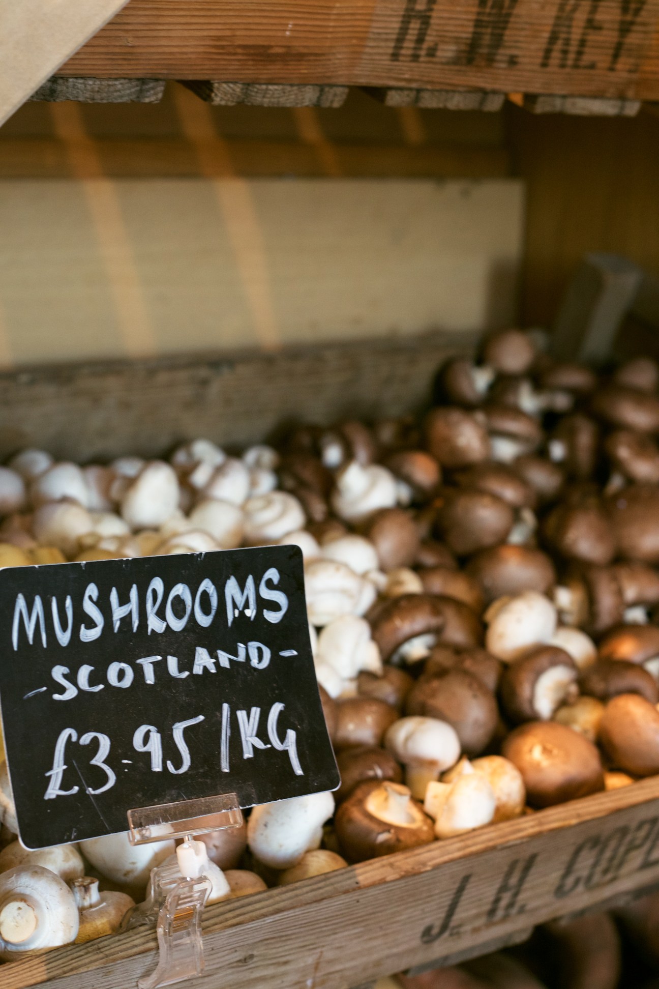 Scottish mushrooms displayed in a wooden crate with a handwritten price label at £3.95 per kilogram.
