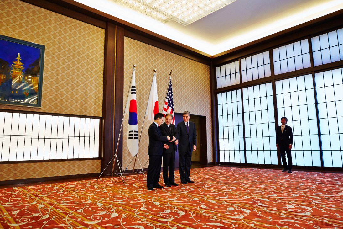 Diplomats from Japan, South Korea, and the US converse at Iikura Guest House with their national flags displayed.