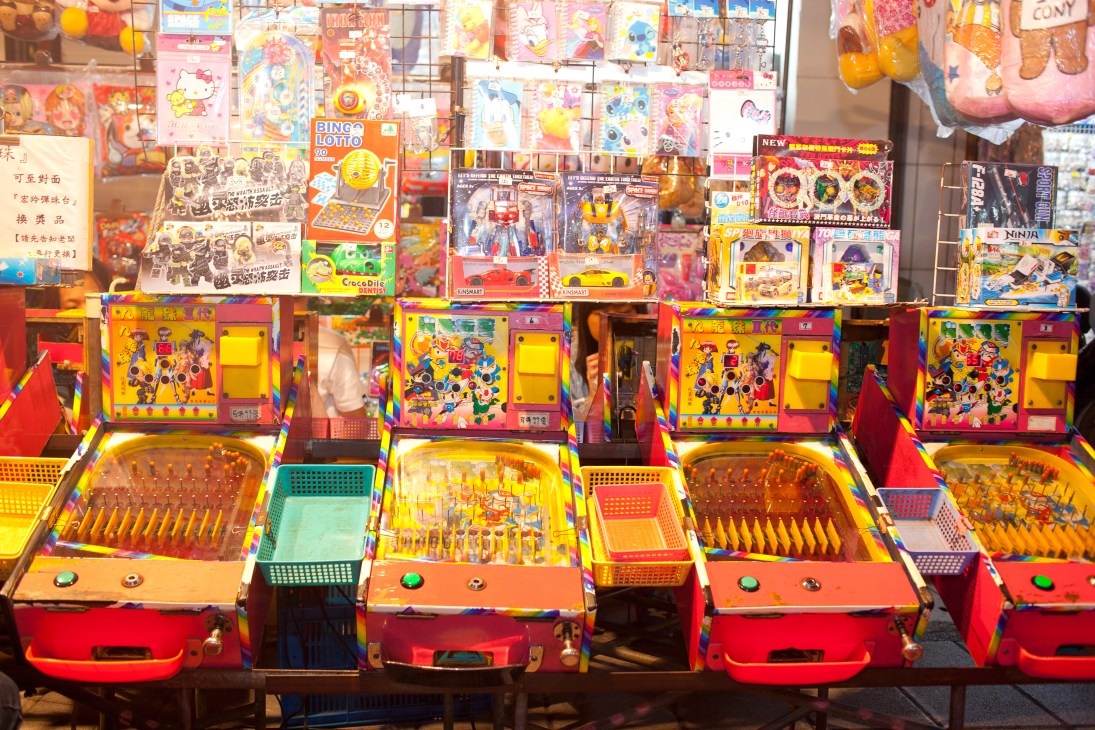 Colorful arcade game machines and prize display booths at a Taipei night market.