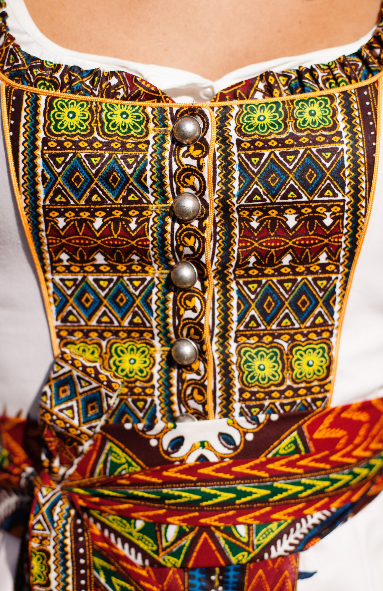 Detail of a colorful Bavarian dirndl bodice featuring geometric patterns in yellow, blue, red and gold with decorative silver buttons.