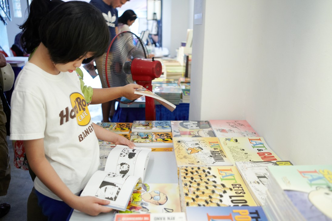 Young girl browsing cartoon books and publications at a festival table display.
