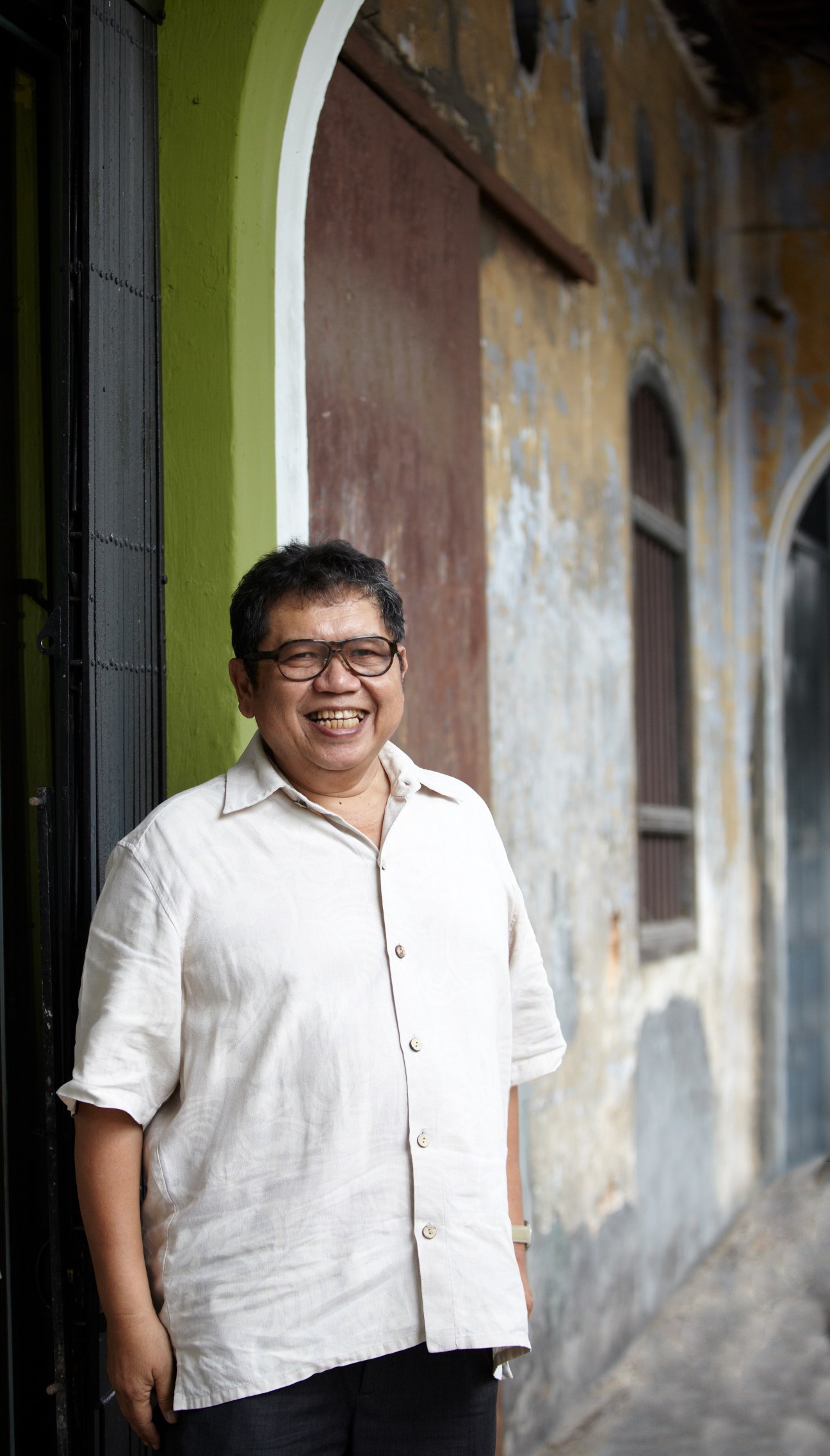 Malaysian cartoonist Mohammad Nor Khalid, known as Lat, smiling in front of a colorful colonial building.