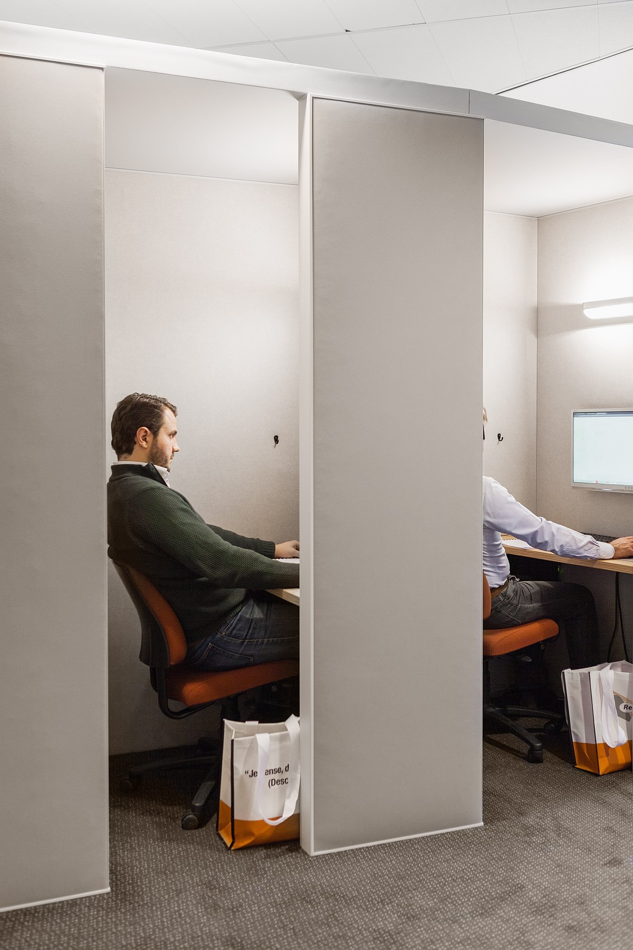 A man in a green sweater sits at a desk in a private study booth at a language school.