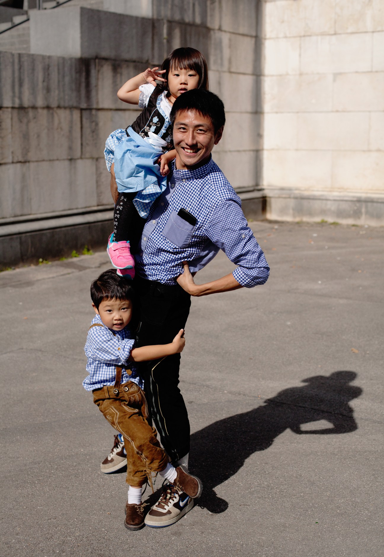 Man and two young children wearing traditional Bavarian tracht with lederhosen and dirndl standing outdoors.