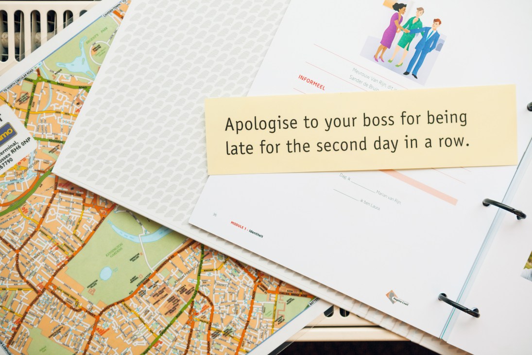 Study materials including maps and lesson books with a sample phrase about apologizing to a boss.