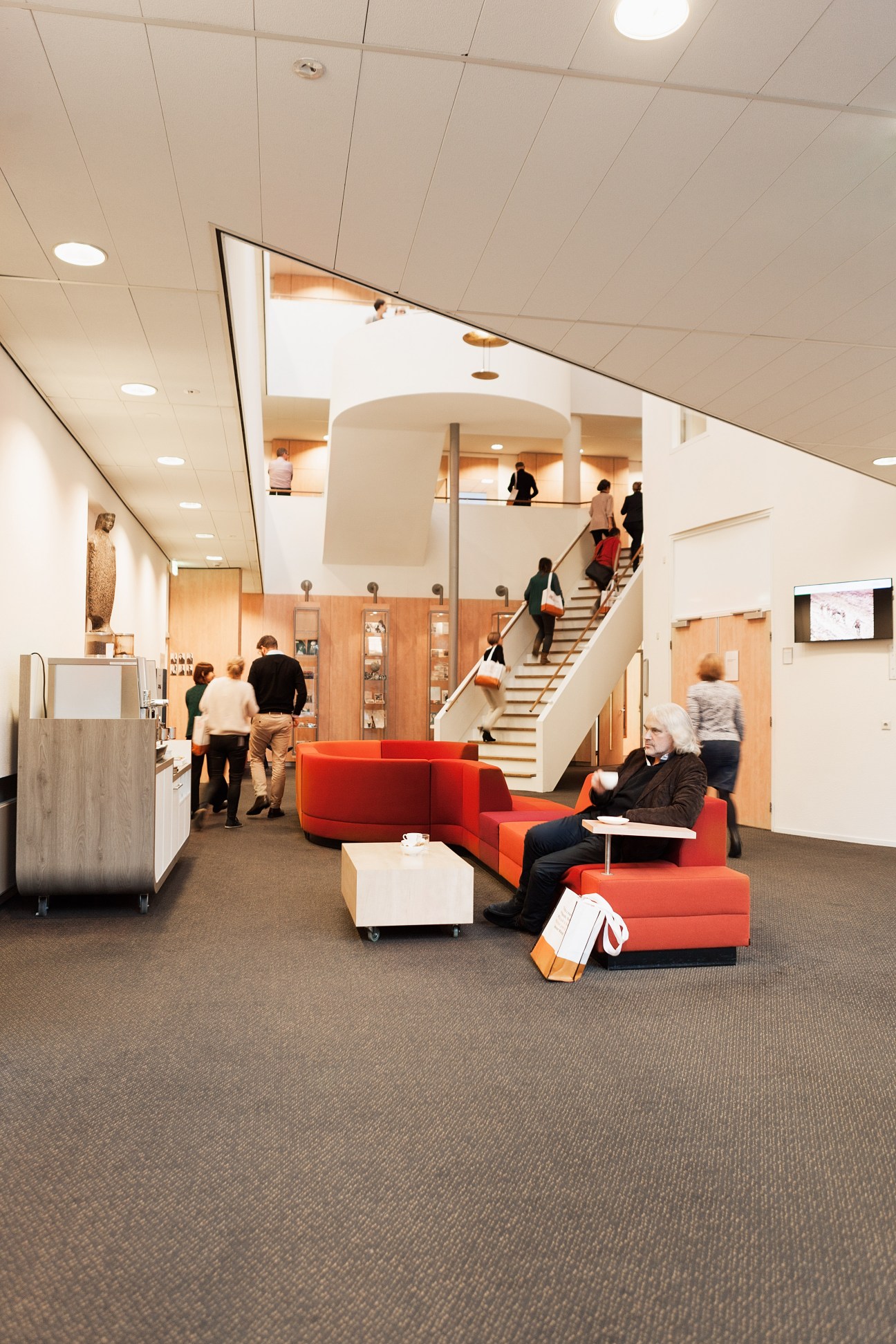 Modern school lobby with red seating, curved architectural elements, and students on stairs.
