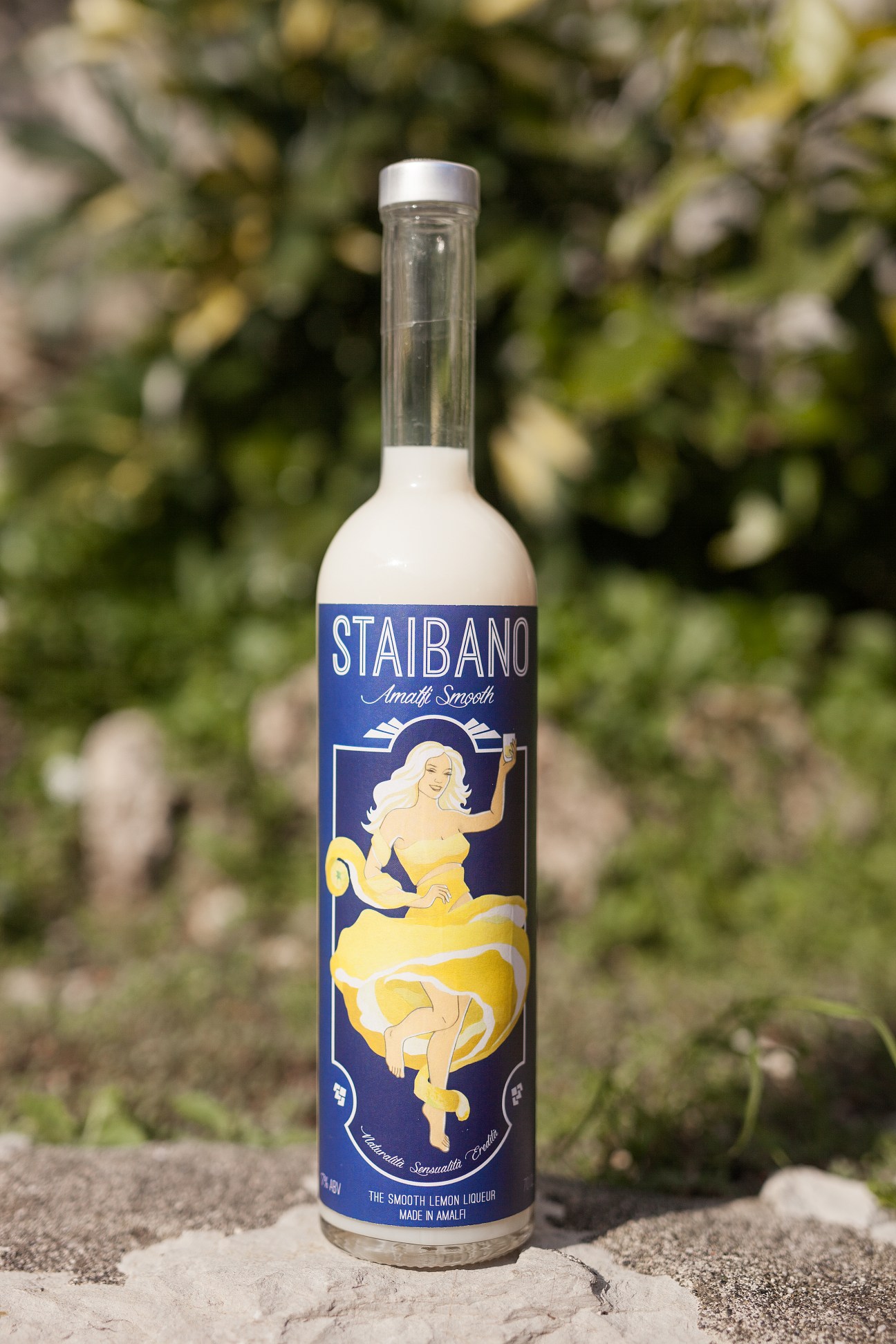 Staibano lemon liqueur bottle with blue label and cream-coloured liquid, displayed against lemon grove foliage.