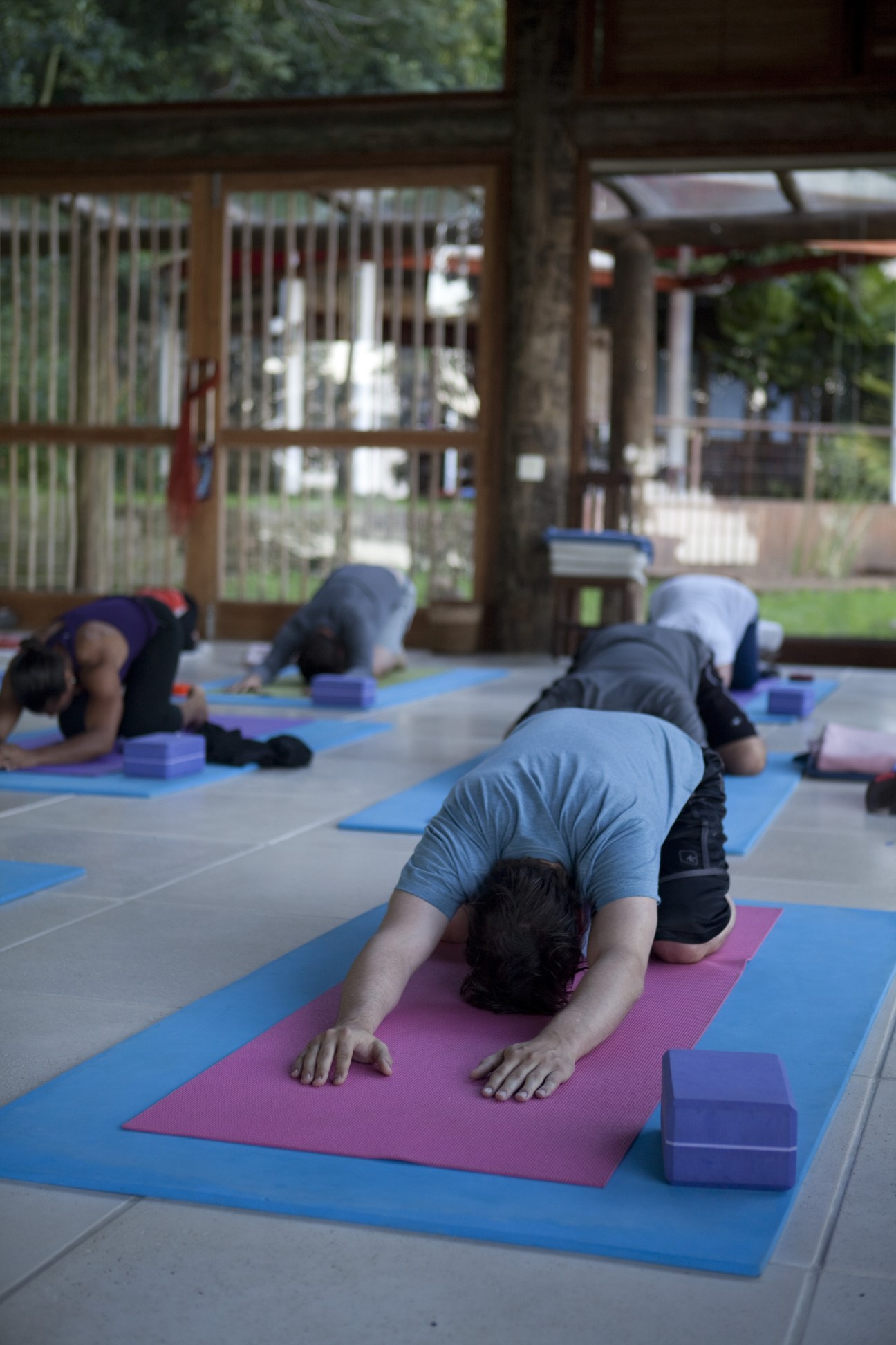 Multiple people practicing yoga in forward fold pose on colorful mats outdoors at The Island Experience in Brazil.