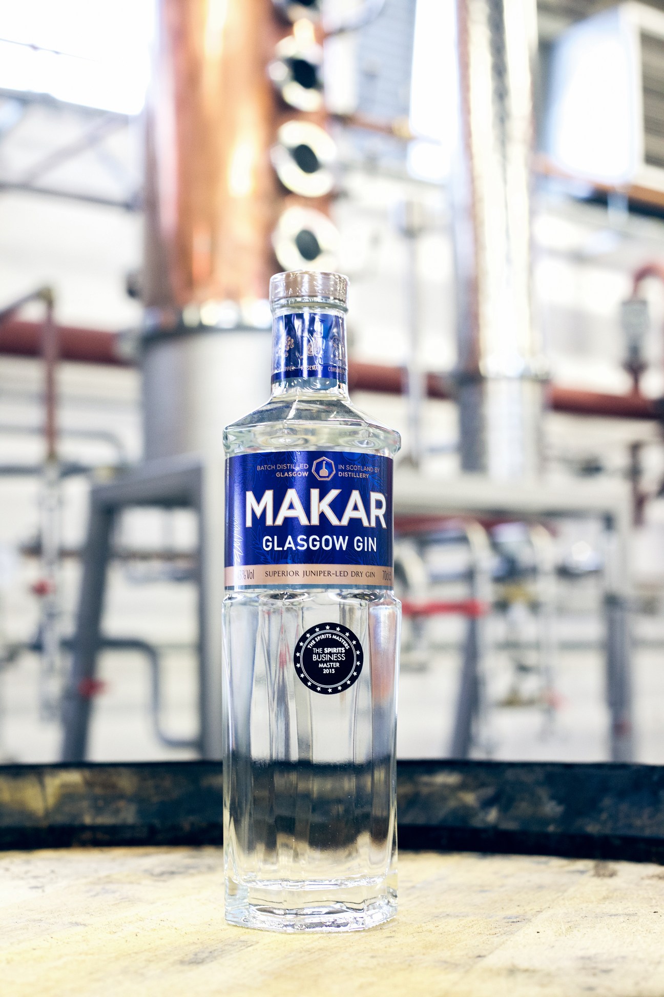 Bottle of Makar Glasgow gin with blue label positioned in front of distillery equipment
