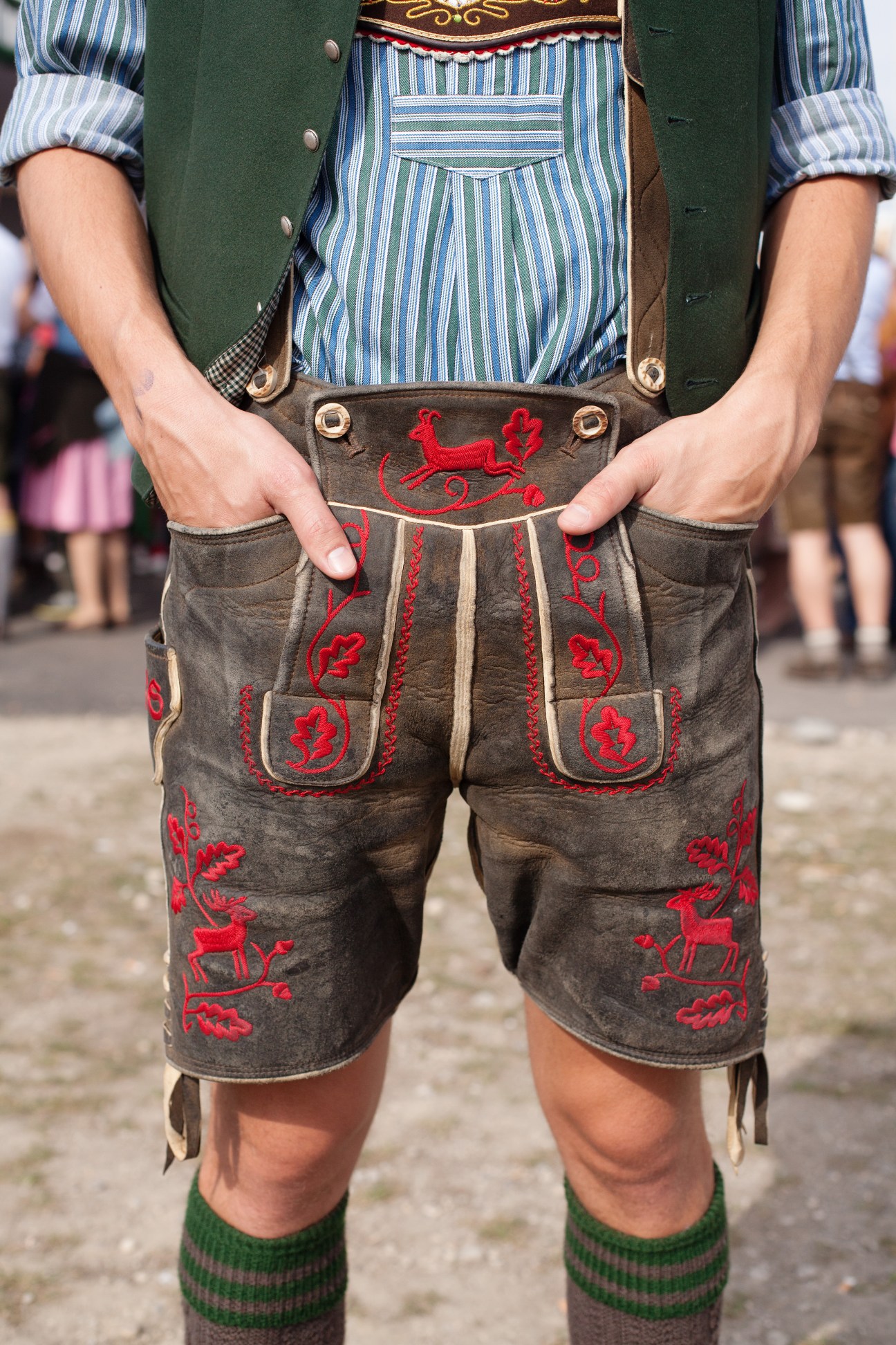 Young man wearing traditional Bavarian lederhosen with red embroidered deer motifs and a green jacket at Oktoberfest.