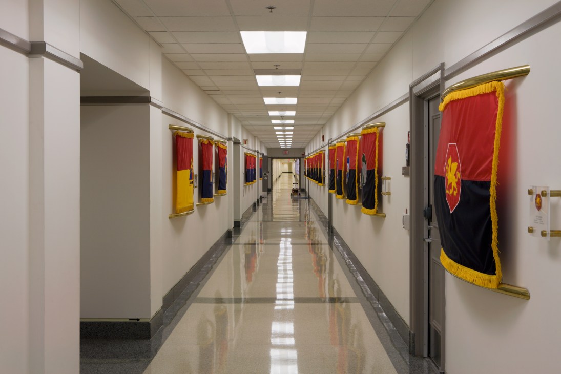 Long Pentagon corridor with polished floor and National Guard flags with red, yellow, and blue colors hanging on walls.
