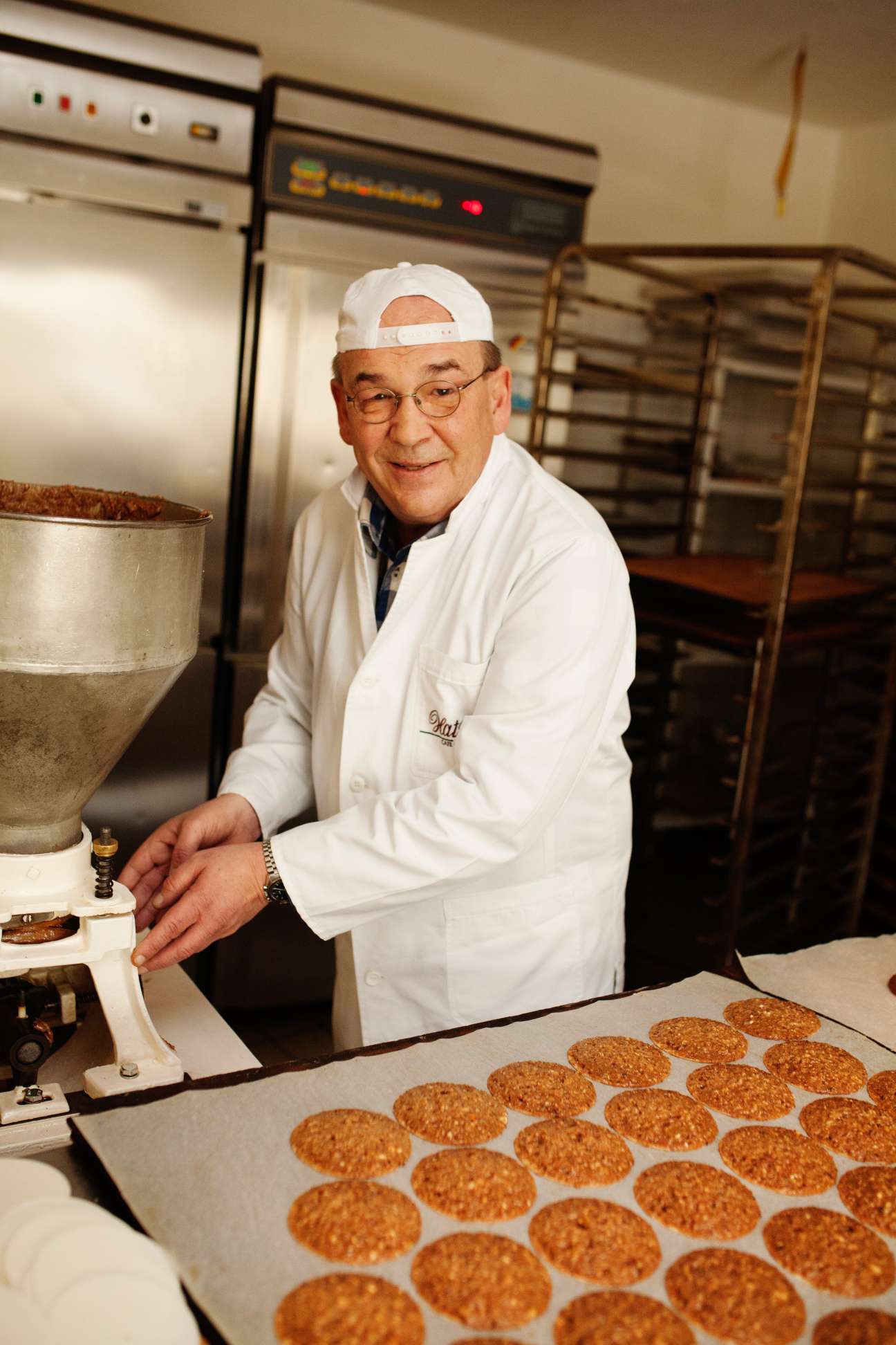 Baker in white coat and headband at Hatzel gingerbread factory with freshly baked elisenlebkuchen biscuits.