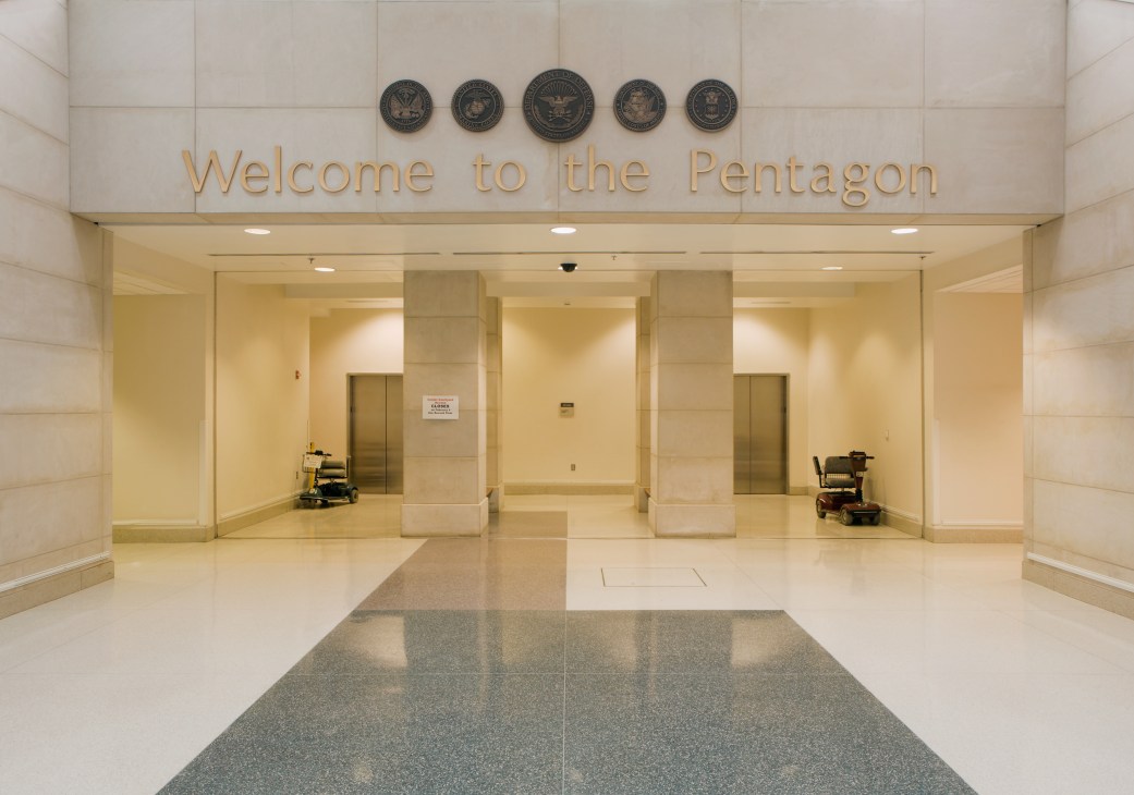 Pentagon entrance hall with 'Welcome to the Pentagon' sign and military seals above elevators.
