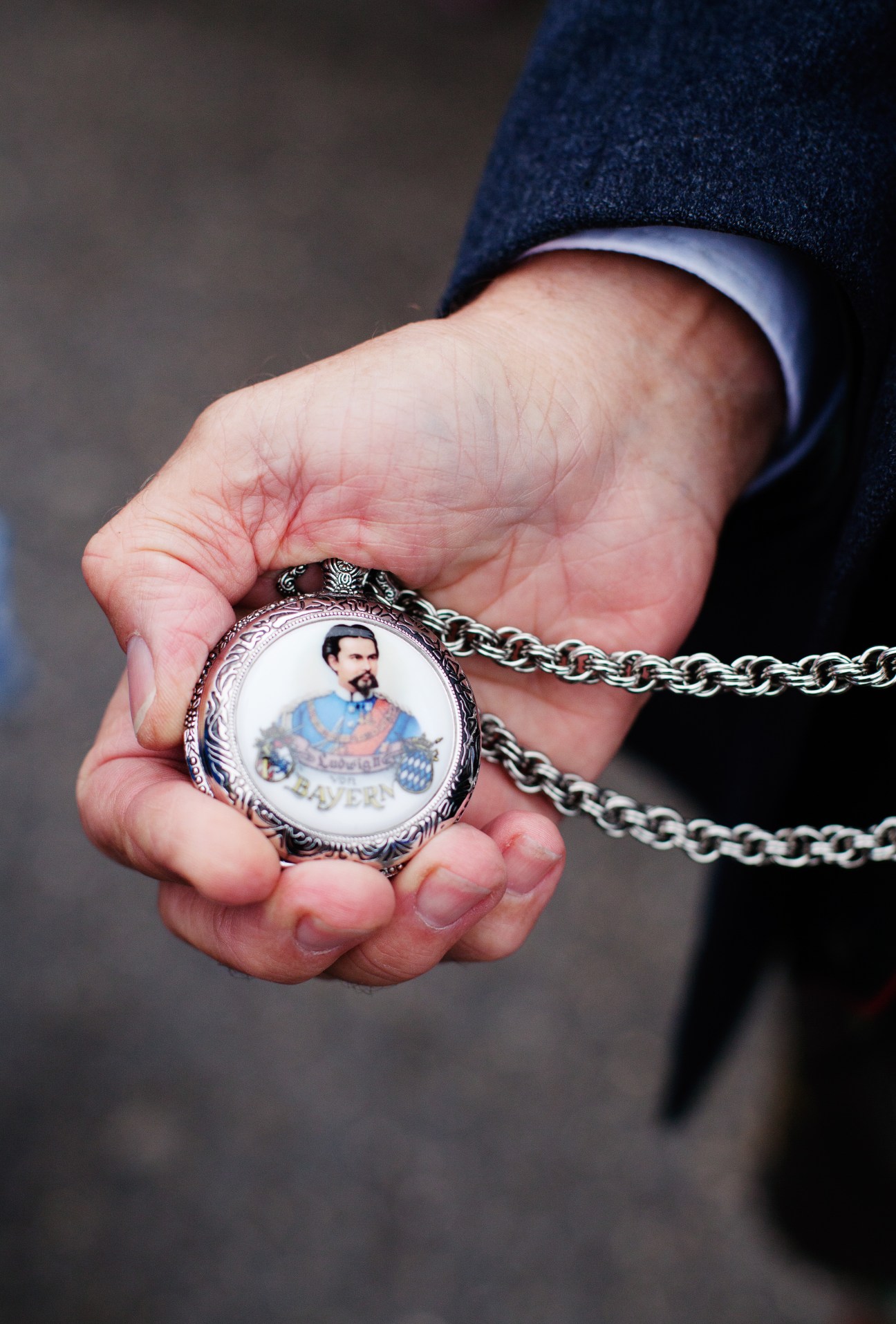Hand holding a decorative pendant featuring King Ludwig II's portrait on a metal chain.