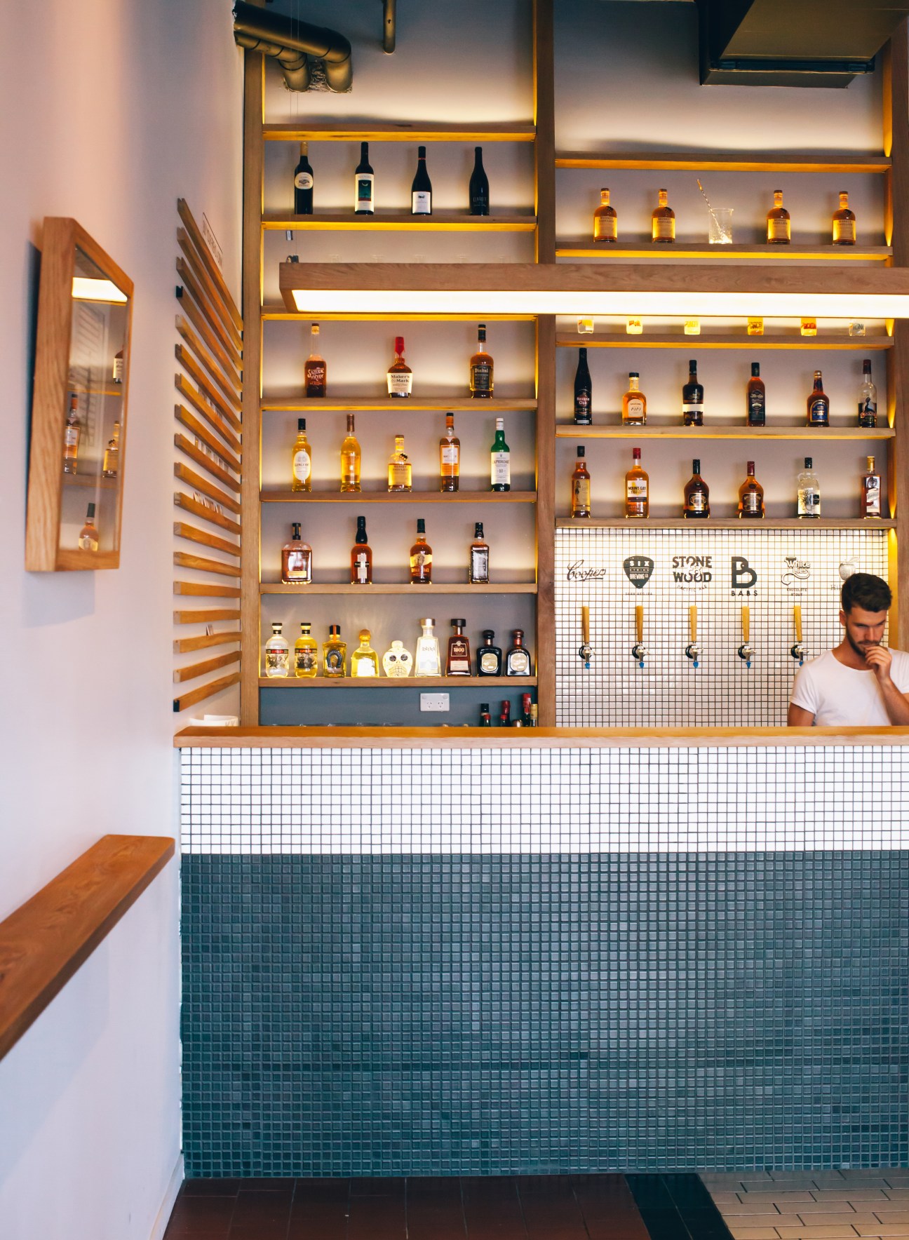 Barbara bar in Brisbane with illuminated shelving displaying spirits and a bartender at the white tile counter.