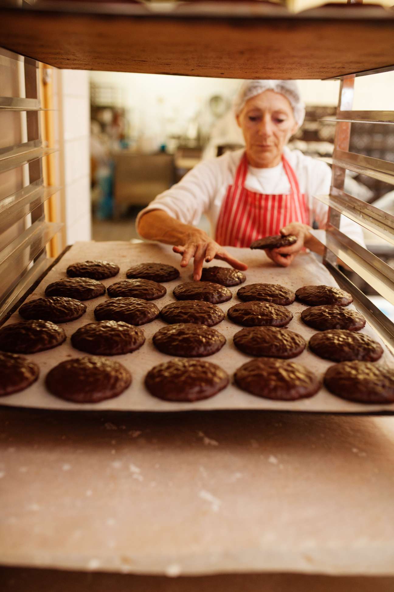 Baker in red apron arranging freshly baked gingerbread cookies on parchment paper inside an oven at Hatzel bakery.