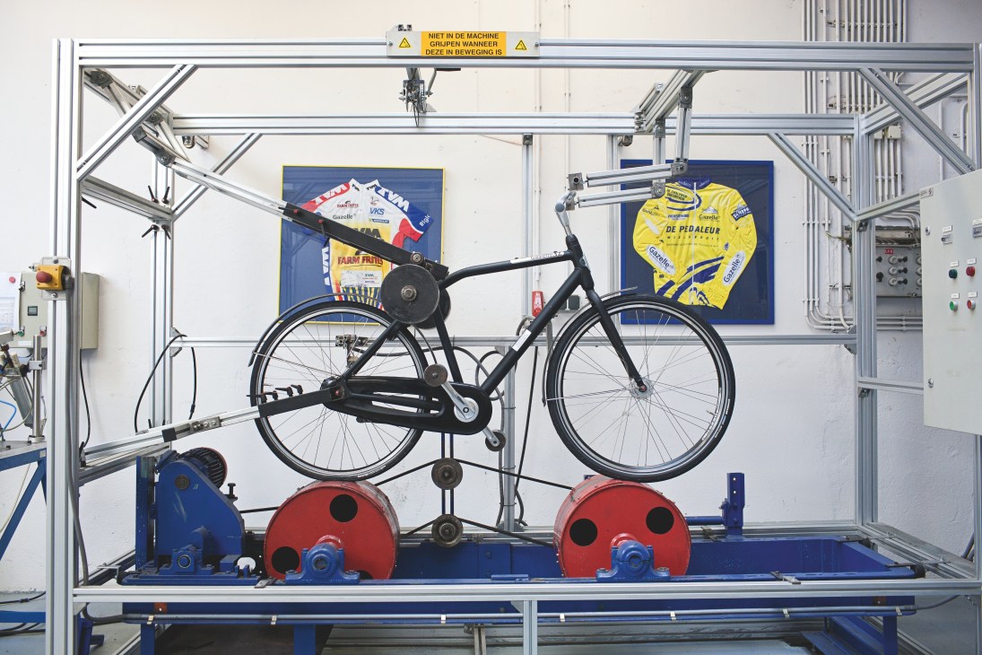 Black Gazelle bicycle on testing equipment with red weights in a factory production line.