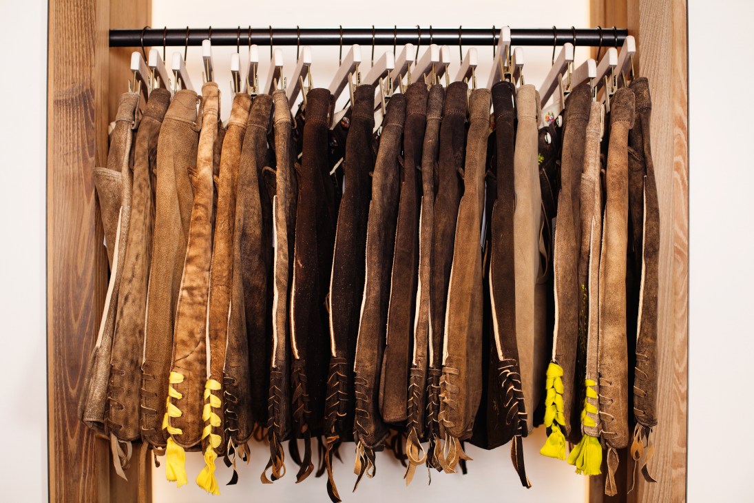 Multiple pairs of brown leather lederhosen and traditional trousers hung on hangers at Lodenfrey shop.