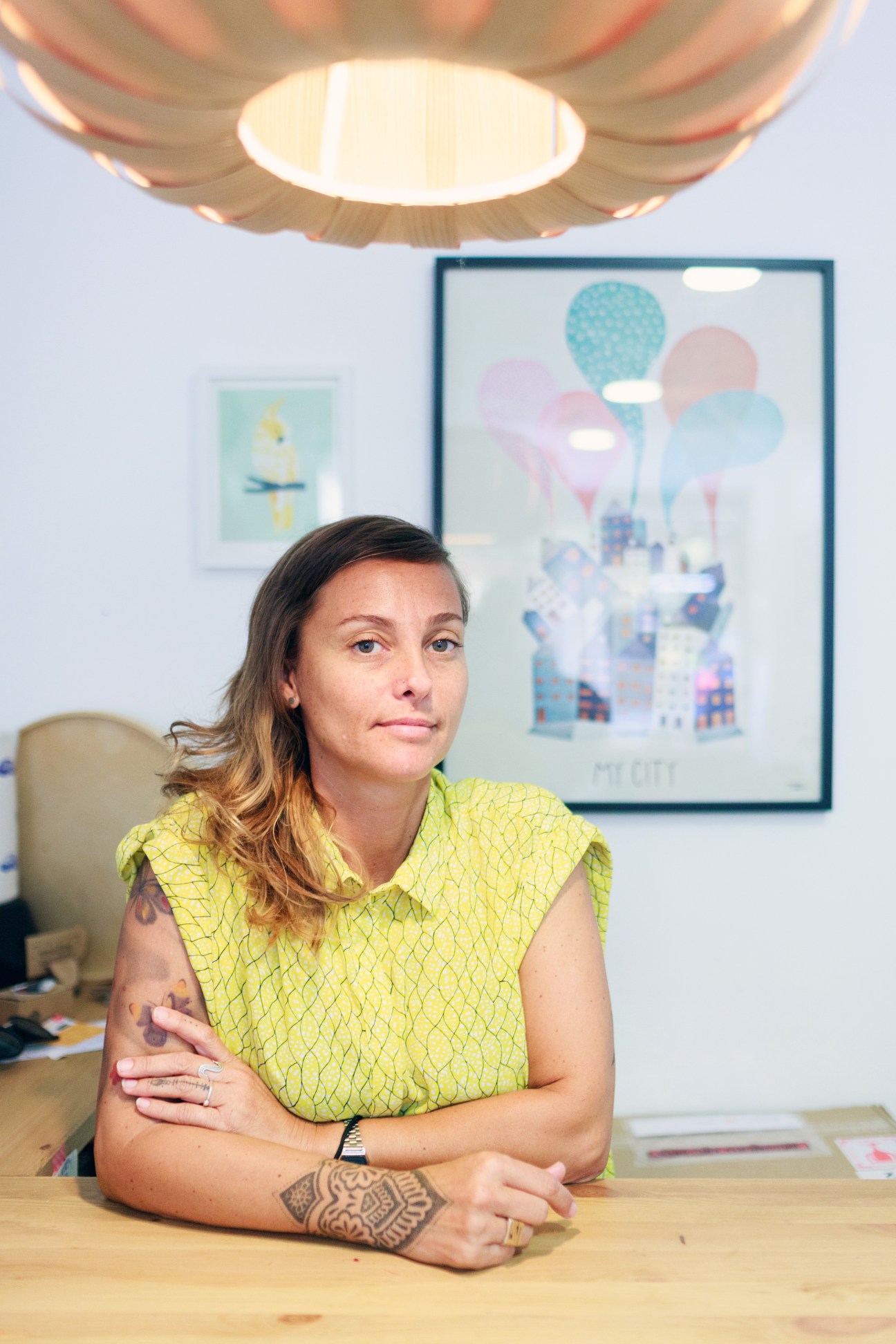 Woman in yellow sleeveless top sitting at wooden desk in modern office with artwork on wall