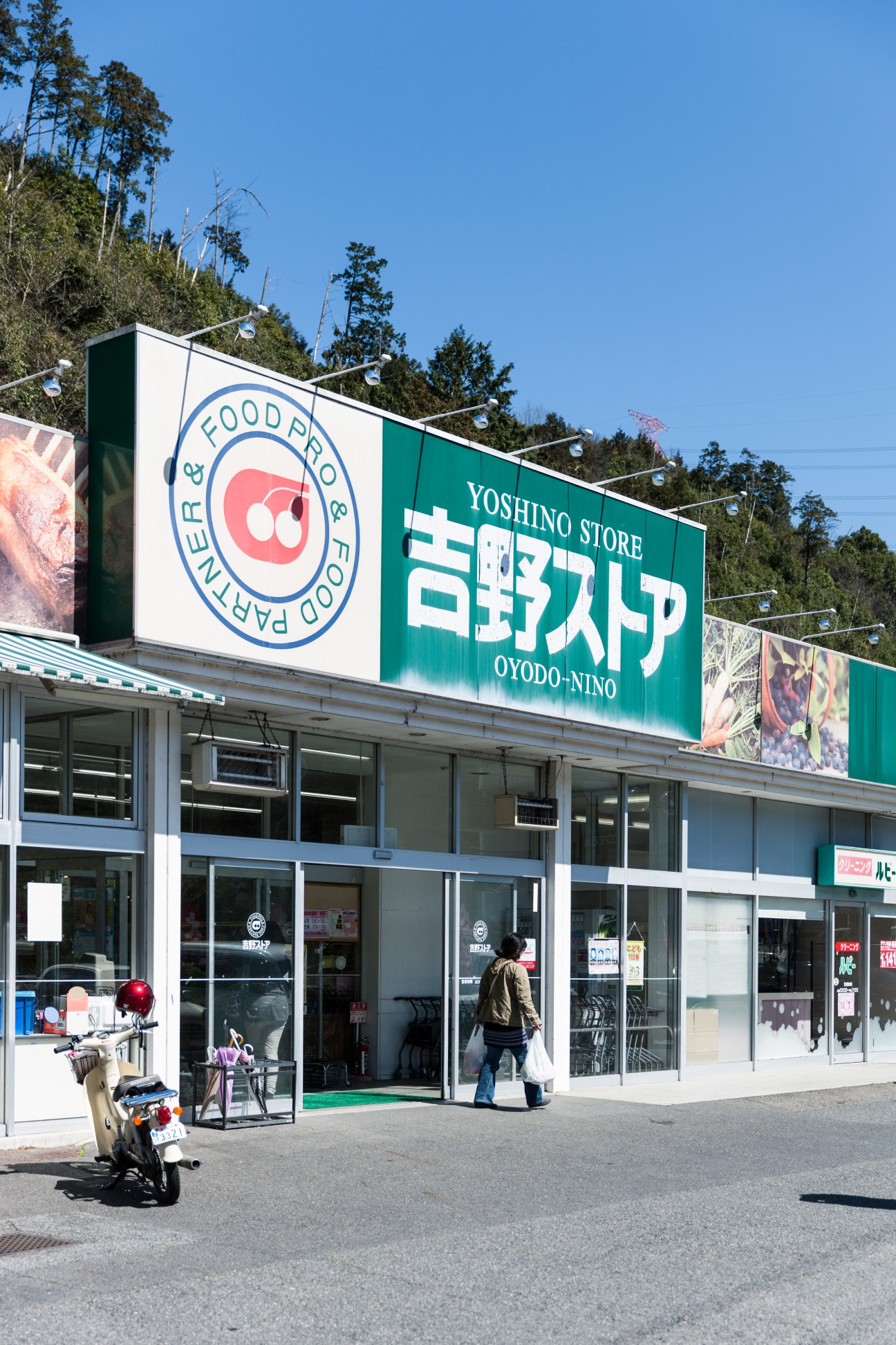 Yoshino Store storefront in Nara, Japan, with green signage and Japanese characters, a customer entering, and a scooter parked outside.